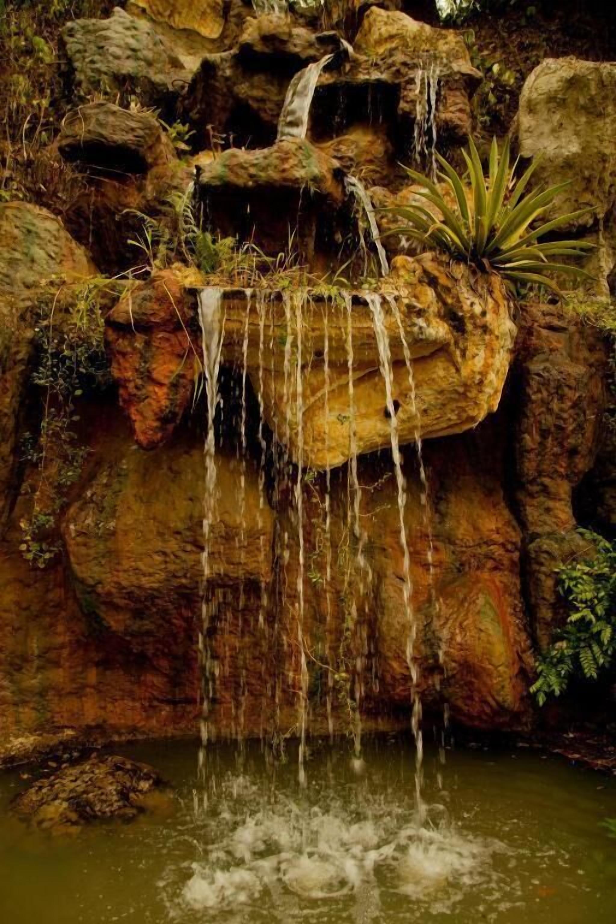 A waterfall cascading over rocks into a pool, surrounded by greenery.