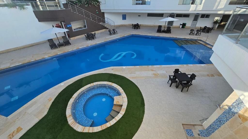 A swimming pool with a decorative design, surrounded by a patio area with outdoor seating and a small circular hot tub.