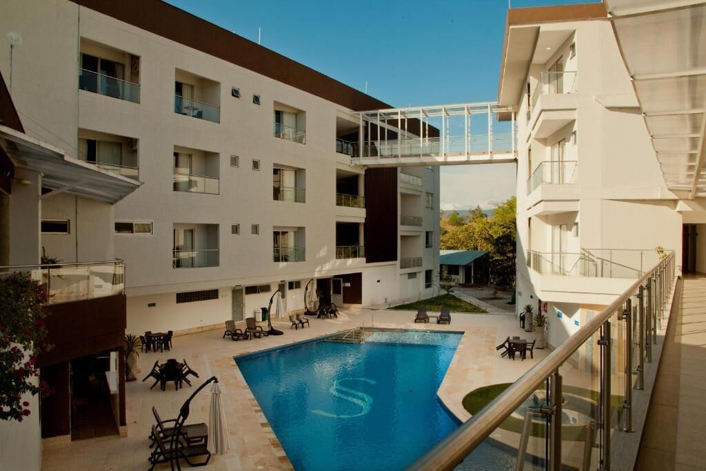 A modern building with a swimming pool, outdoor seating, and a glass bridge connecting different levels.