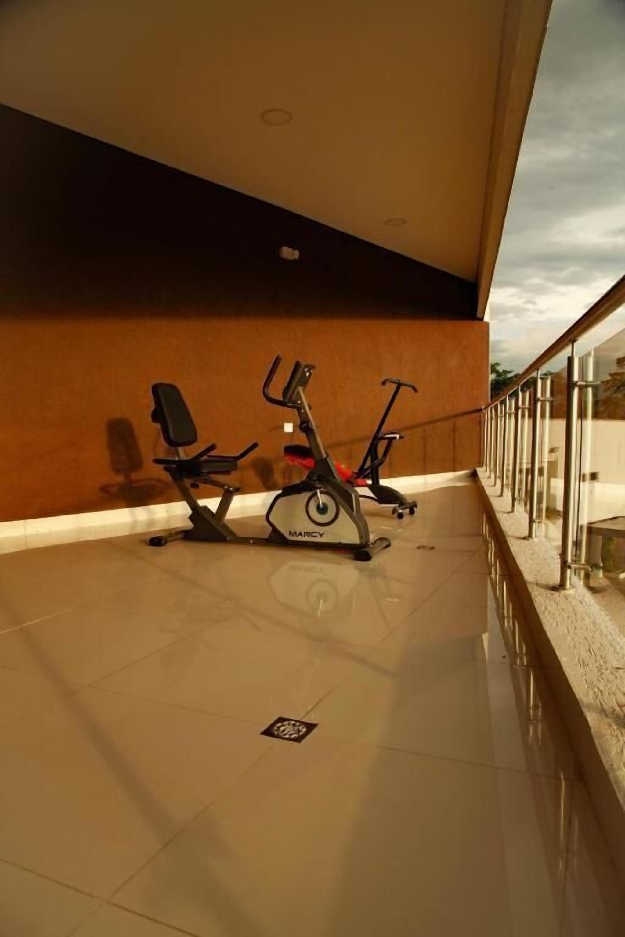 Un área de ejercicio interior con dos bicicletas estáticas y un banco, suelo de baldosas y barandilla de vidrio.