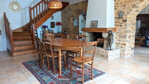 Un comedor con mesa y sillas de madera, un tapete estampado, una chimenea de piedra y una escalera de madera.