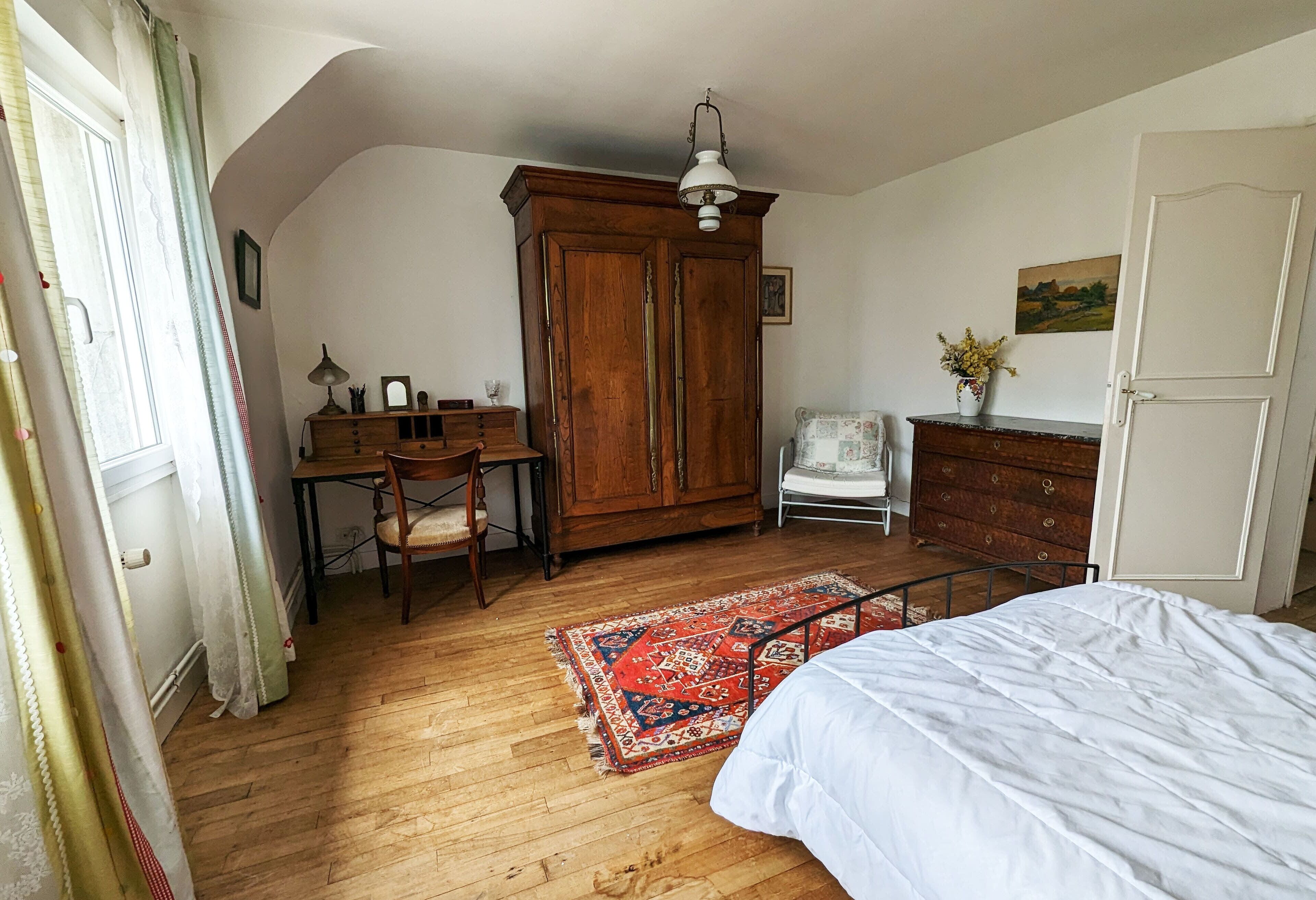 Ein Schlafzimmer mit einem Holzschrank, einem Schreibtisch mit Stuhl, einem Bett und einem roten Teppich mit Muster.