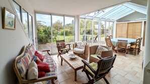 Una habitación soleada con sofá, sillas y una mesa, con grandes puertas de vidrio que dan a un jardín.
