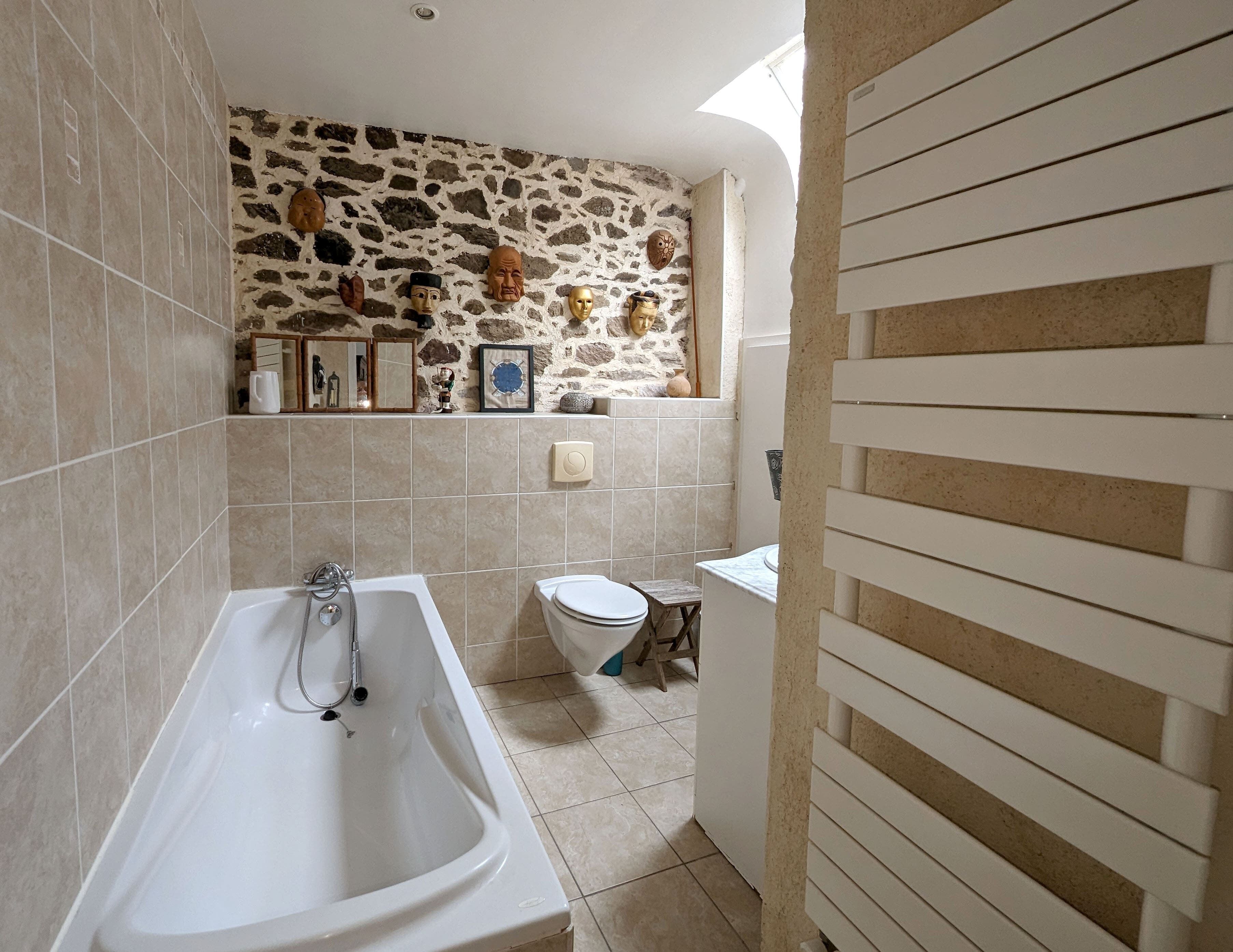 A bathroom with a stone wall, a bathtub, a toilet, and a sink.