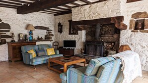 Un salón acogedor con chimenea de piedra, sofás estampados, una mesa de centro de madera y un televisor.
