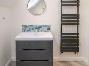 A bathroom with a white sink, a blue-tiled backsplash, a round mirror, and a dark towel rack. - The Caradoc (Shrewsbury)