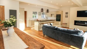 A modern kitchen with an island, a dining area with a wooden table, and a living room with a grey sofa. - The Caradoc (Shrewsbury)