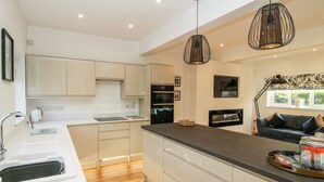 A modern kitchen with white cabinets, a wooden countertop, and a built-in oven. There are pendant lights and a window with a view of greenery. - The Caradoc (Shrewsbury)