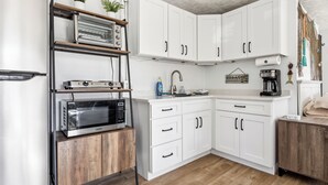 Una cocina moderna con armarios blancos, horno empotrado, microondas y cafetera.