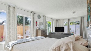Un dormitorio con cama, televisor, sofá y ventana con cortinas.