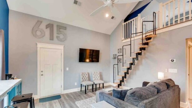 A modern living room with a staircase, a sofa, and a TV mounted on the wall.