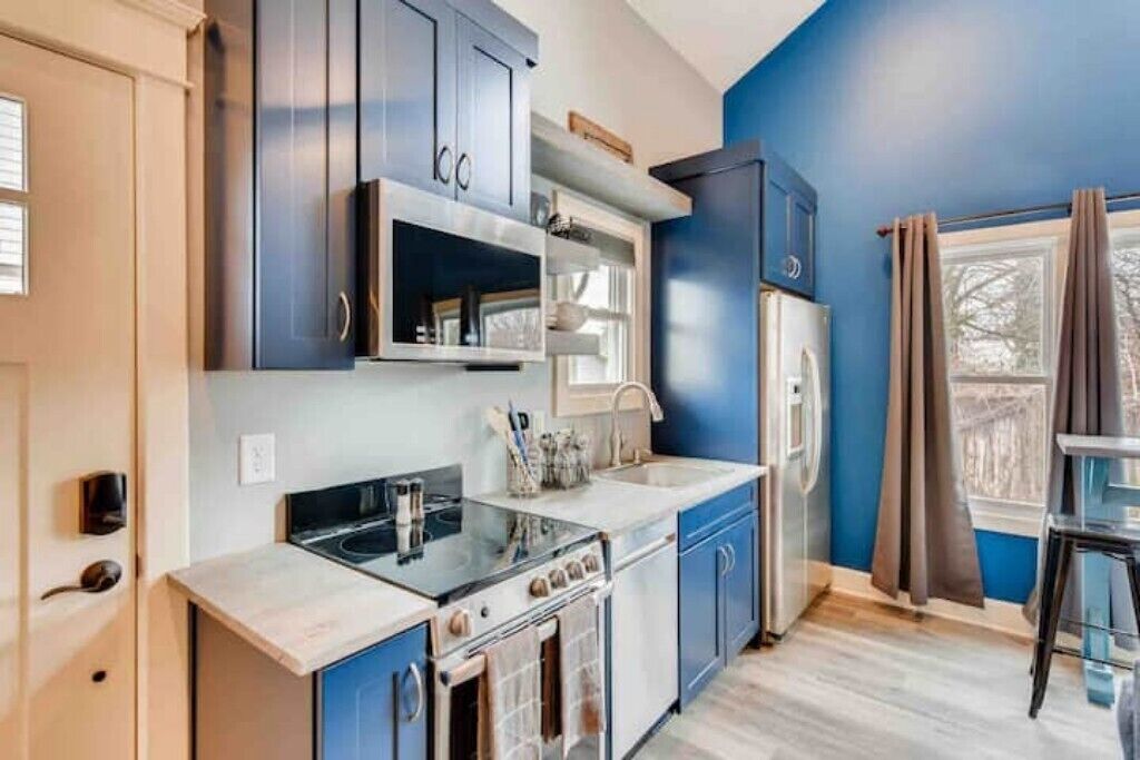 A modern kitchen with blue cabinets, a stainless steel refrigerator, and a built-in oven.