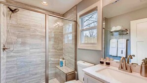 A modern bathroom with a glass-enclosed shower, a toilet, a sink with a vanity, and a window providing natural light.