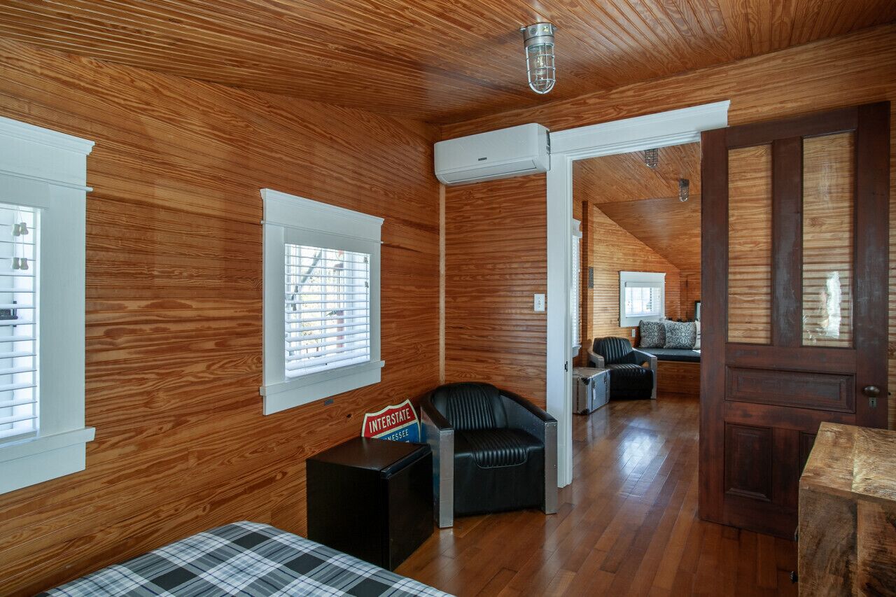A room with wooden walls and a ceiling, a black leather chair, a wooden bench, and a door.