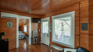 Interior acogedor de una cabaña con paredes de madera, una cama, una mesita y un ventanal con persianas.