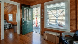 Una habitación con paredes de madera, una puerta verde, una ventana con persianas, una cama, una maleta y un sofá.