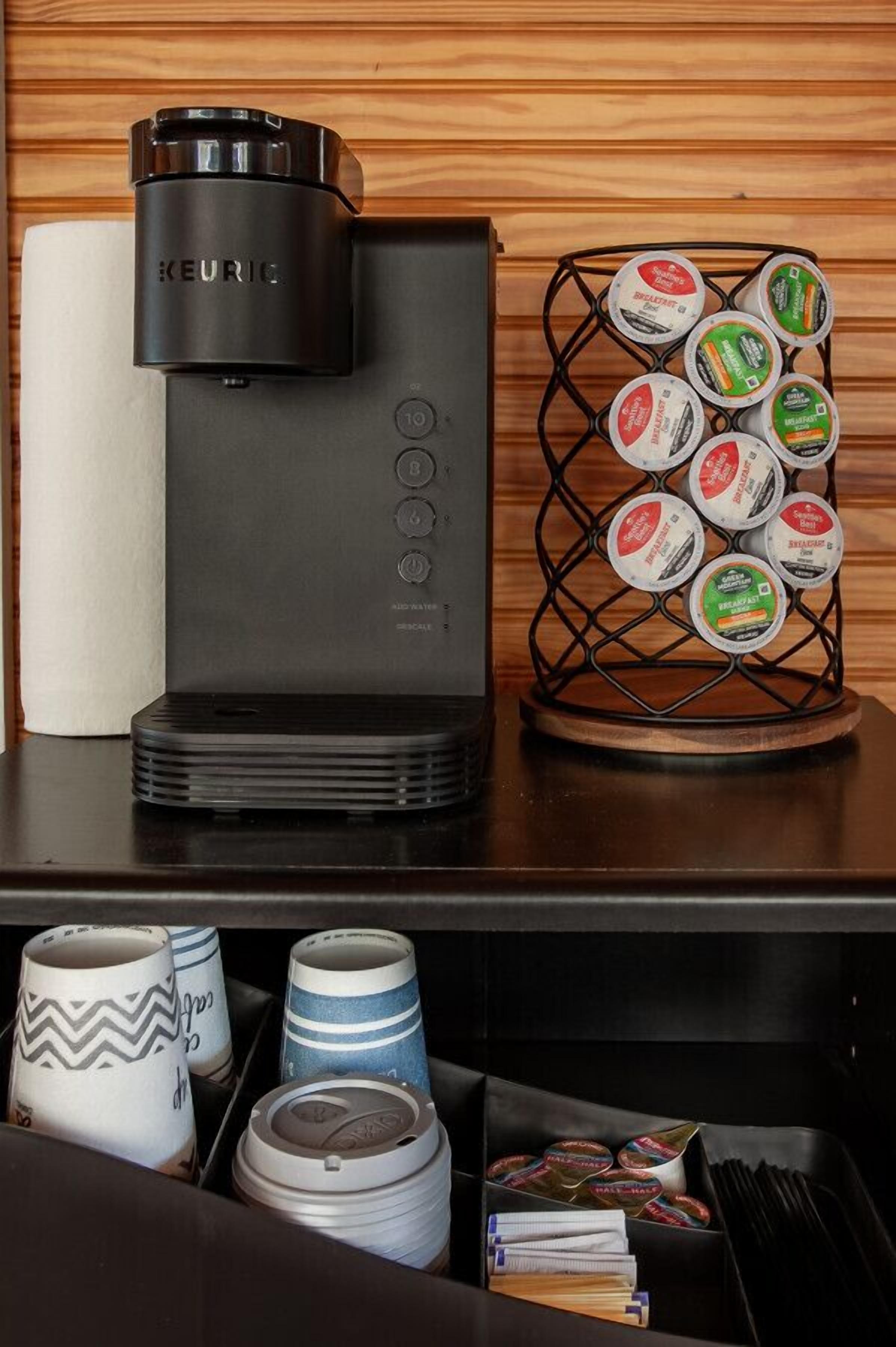 Een Keurig koffieapparaat met een koffiepadhouder en een lade met mokken en bestek.