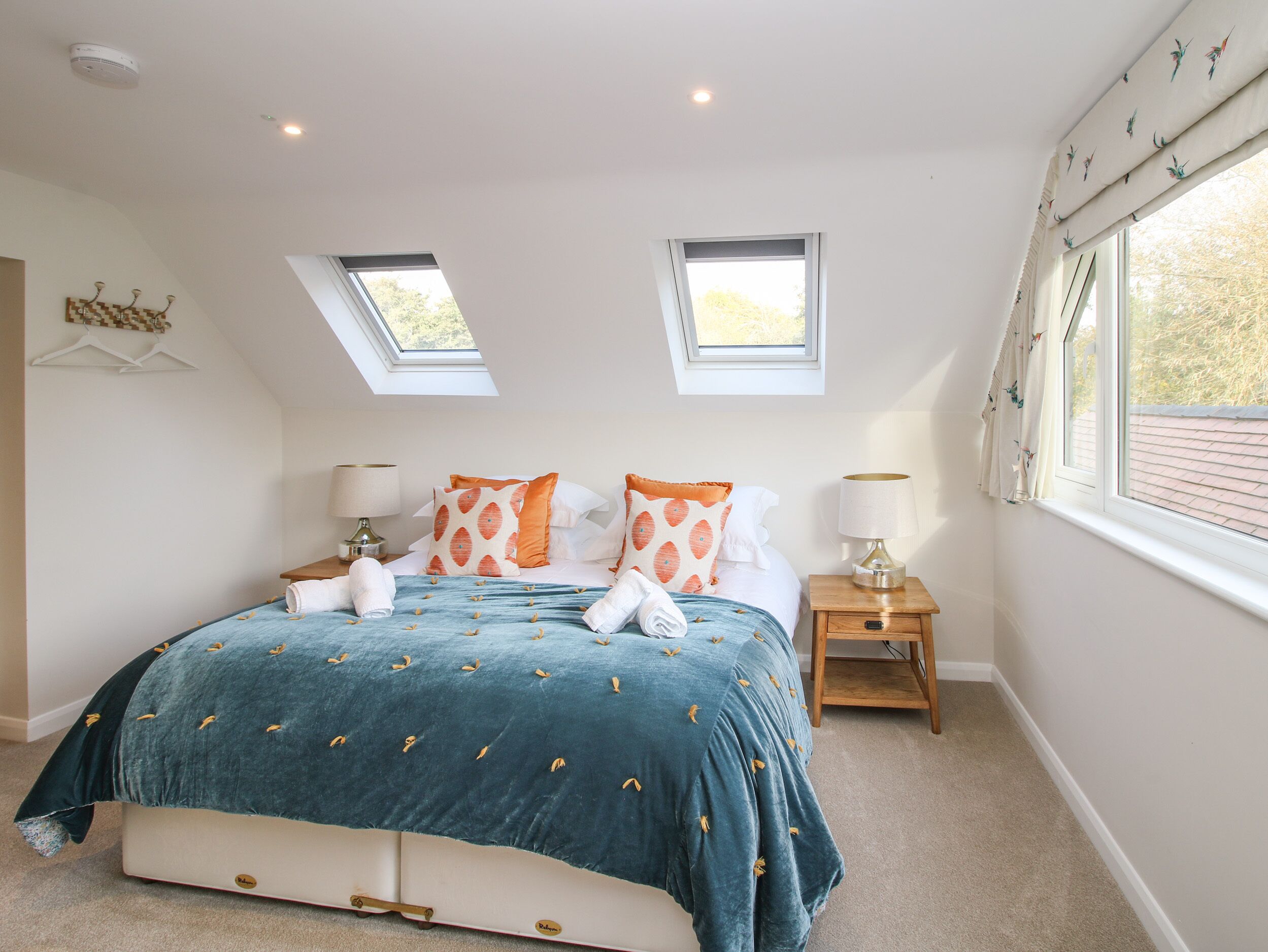 A bedroom with a large bed, two bedside tables, a skylight, and a window with curtains.