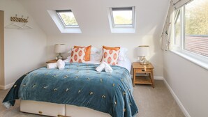 A bedroom with a large bed, two bedside tables, a skylight, and a window with curtains. - The Lawley (Shrewsbury)