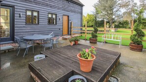 A wooden house with a patio area featuring a table and chairs, potted plants, and a wooden fence. - The Lawley (Shrewsbury)