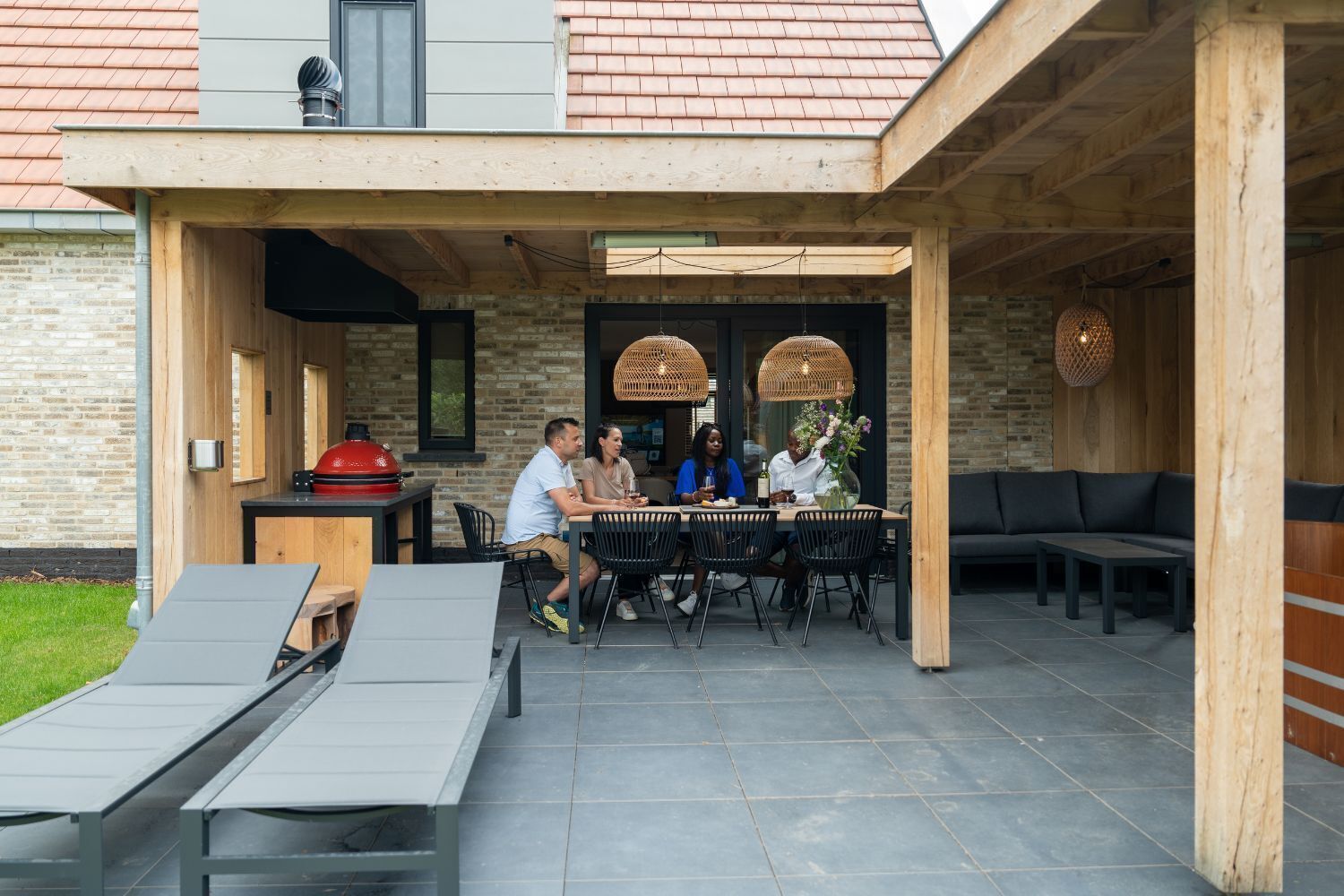 Eine Terrasse im Freien mit Esstisch und Stühlen, einem Grill und einer Sitzgruppe mit Sofa und Liegestühlen.