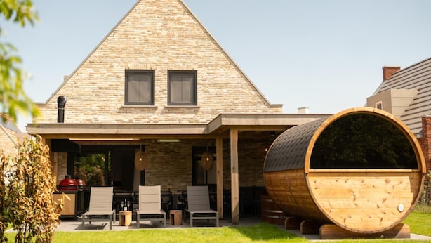 Een huis met een gevel van natuursteen, een zadeldak en een groot houten vat op de voorgrond.