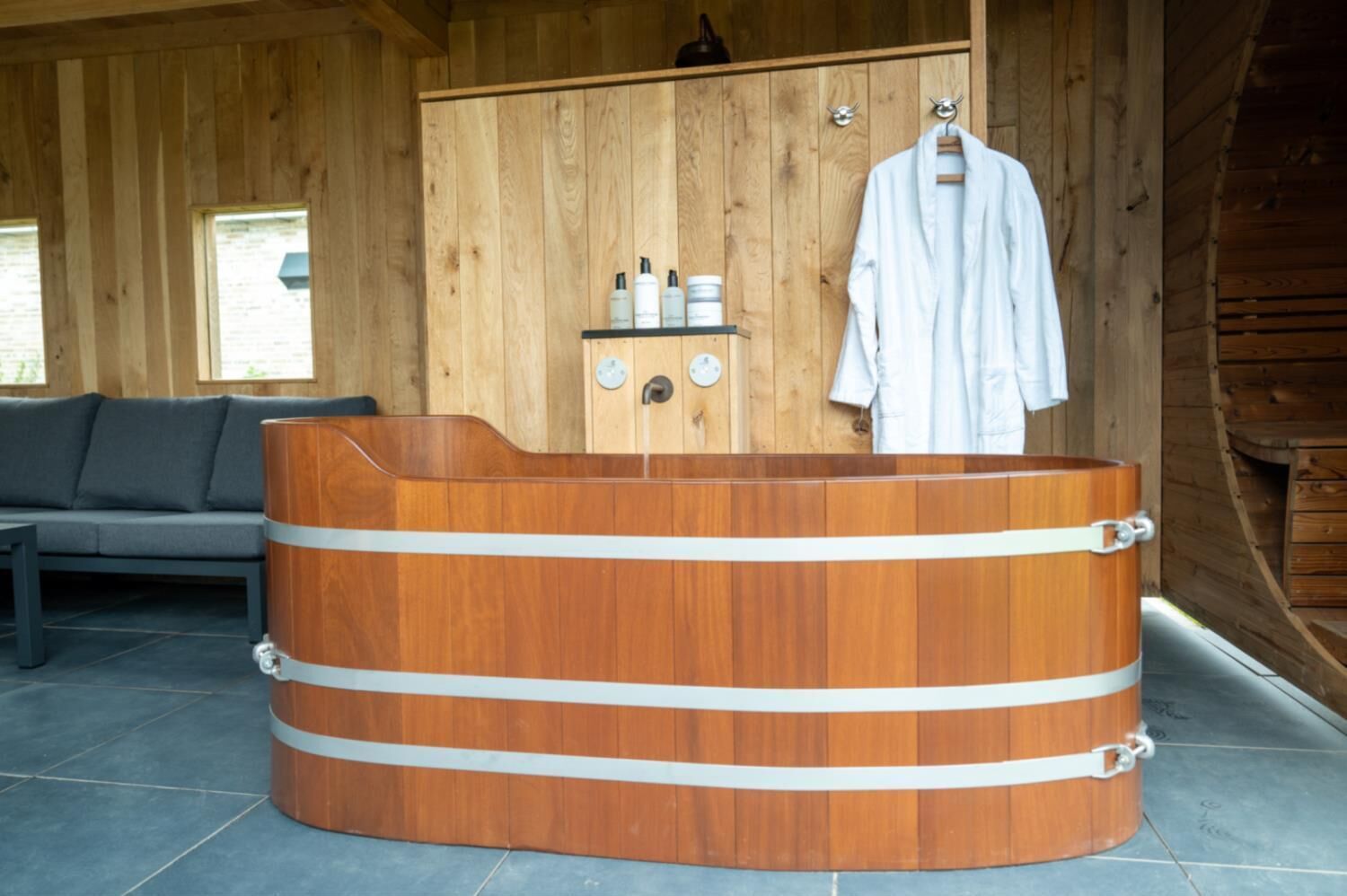 A wooden sauna with a bench, a shelf with bottles, and a white robe hanging on hooks.