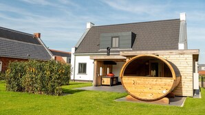 Una casa moderna con una gran estructura de barril de madera, una chimenea y un césped bien cuidado.