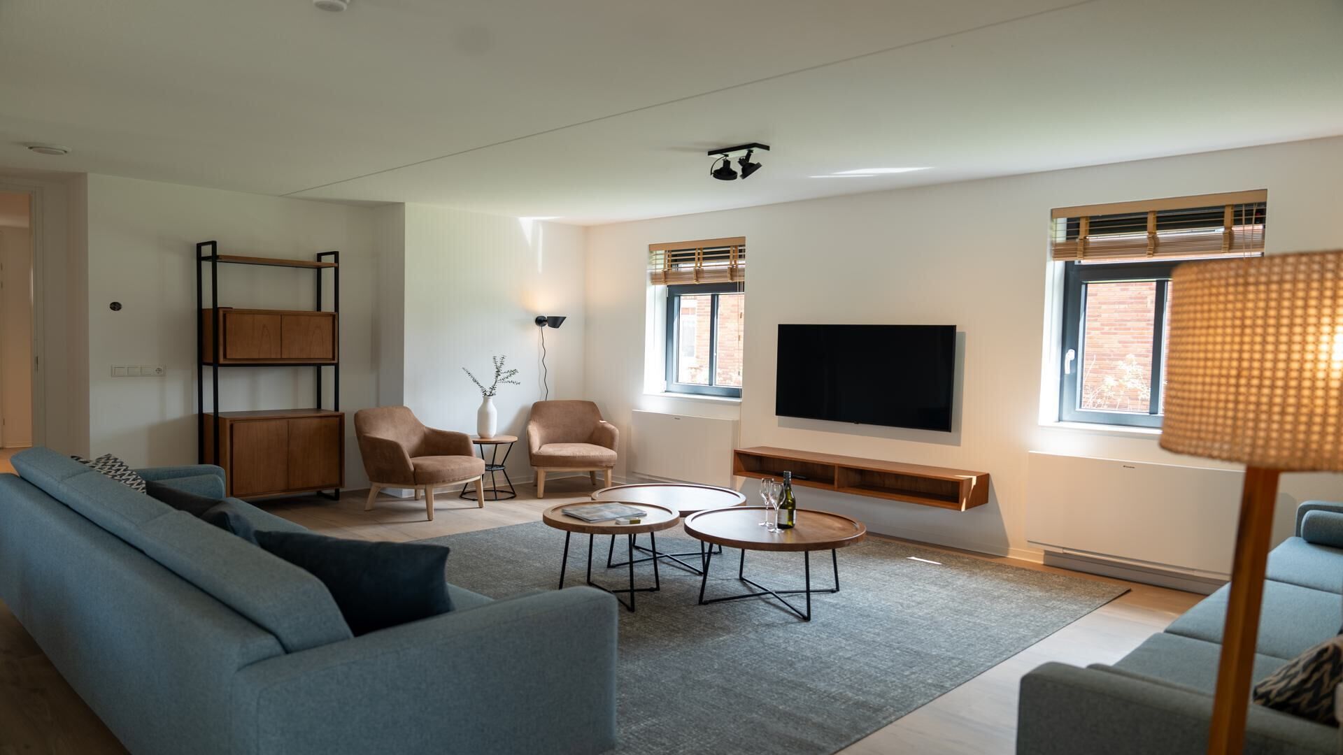 A modern living room with a sofa, two armchairs, a coffee table, a TV, and a lamp.