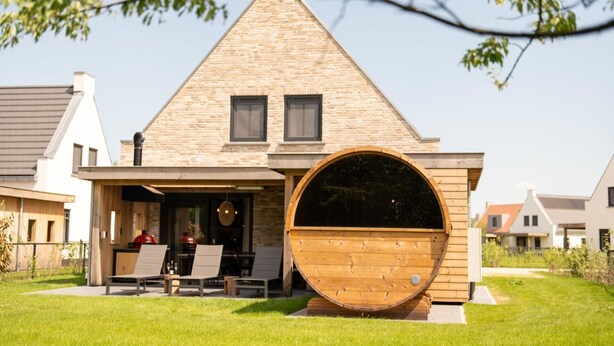 Una casa con un gran ventanal de madera, un espacio de estar techado al aire libre y un césped cuidado.