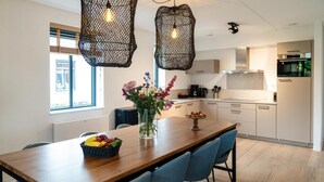 Una cocina moderna con una mesa de comedor de madera, sillas azules, luces colgantes y un florero con flores.