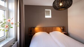 Et soveværelse med sengegavl i træ, et natbord med lampe og et vindue med udsigt.
