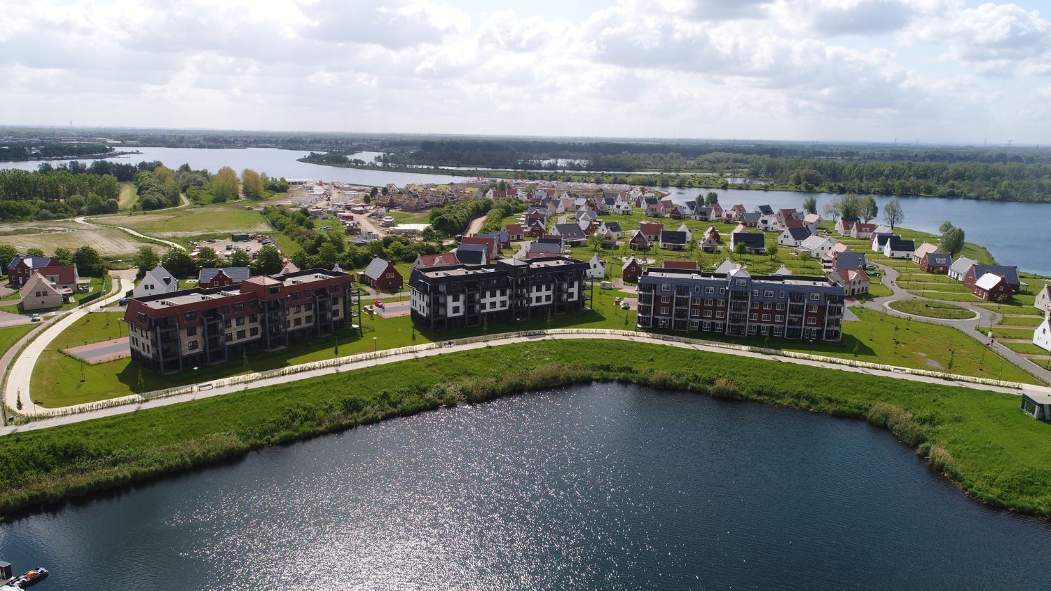 An aerial view of a lakeside residential area with modern buildings, a well-maintained grassy area, and a calm lake.