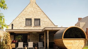 Une maison avec un toit triangulaire, un tonneau en bois et un espace salon extérieur.
