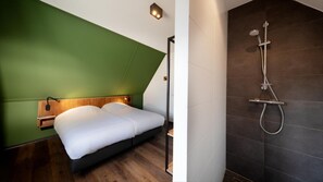 Une chambre d’hôtel moderne avec un lit, un mur d’accent vert et un espace douche aux carreaux foncés.