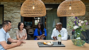 A group of people seated at a wooden table with a bottle of wine and a vase of flowers.
