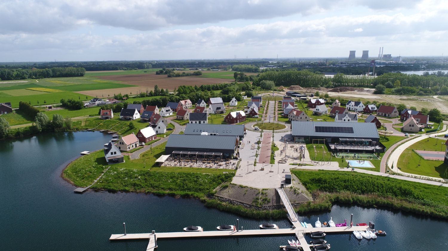 Vista aérea de un pueblo a orillas de un lago, con casas, un muelle y un edificio grande con techo moderno.