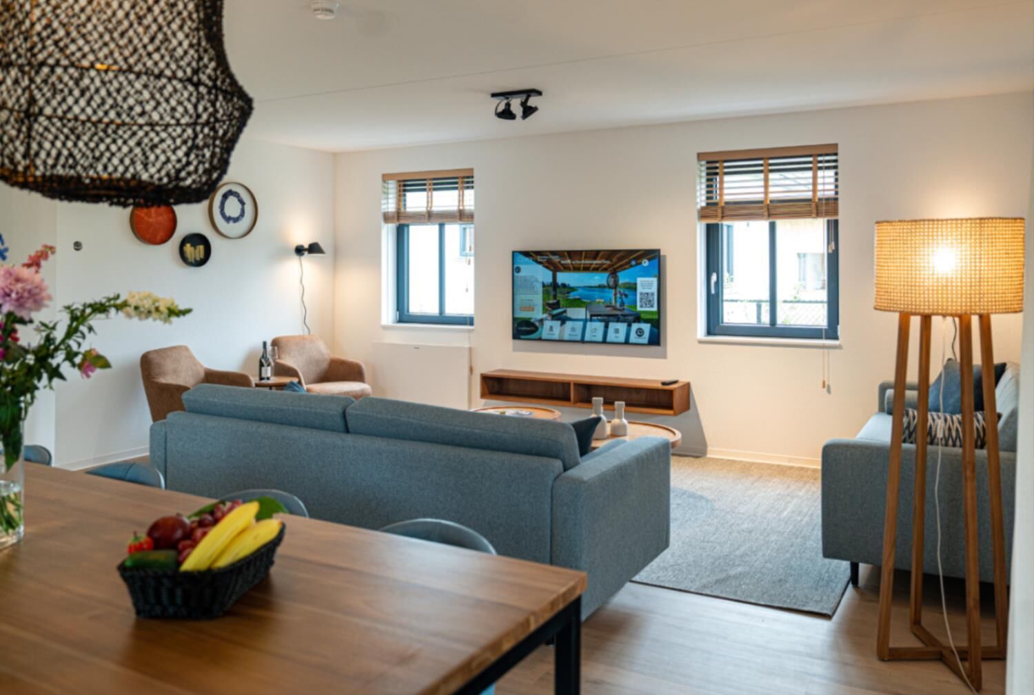 Un salon moderne avec un canapé gris, une table basse en bois et un téléviseur fixé au mur.