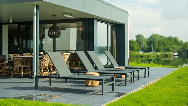 Ein moderner Außenbereich mit Liegestühlen und einem Tisch mit Blick auf ein Gewässer.