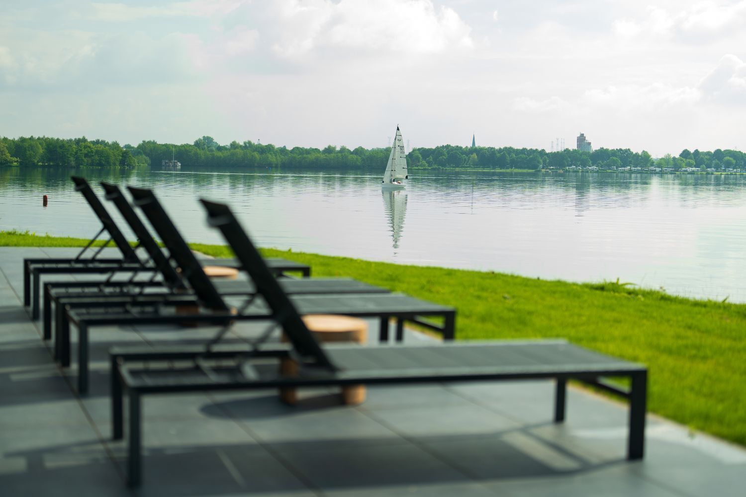 Un espace de détente au bord du lac, avec des chaises longues et un voilier sur l’eau.