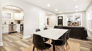 A modern kitchen with white cabinets, a dining area with a table and chairs, and a view of the outside through a window.