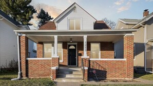 A two-story house with a front porch, brick exterior, and a black front door.