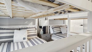 A bunk bed room with striped bedding, a bedside table with a lamp, and a door in the background.