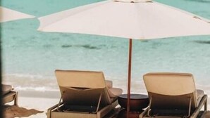 A beach with two lounge chairs and a large umbrella.