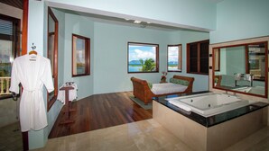 Ein geräumiges Badezimmer mit einer großen Badewanne, Holzboden und Meerblick durch große Fenster.