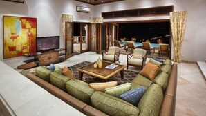 Ein geräumiger Wohnbereich mit einer großen Couch, einem Couchtisch und einem Fernseher. Durch die Glastüren ist ein Pool zu sehen.