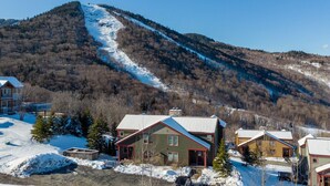 A residential area with houses on a hillside, a ski slope, and a clear blue sky. - SlopeSide- Pool, Grill, Hot tub, Views! (Killington)