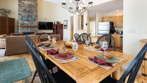 A dining area with a wooden table set for four, surrounded by black chairs. A stone fireplace and a television are visible in the background. - SlopeSide- Pool, Grill, Hot tub, Views! (Killington)
