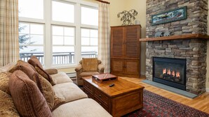 A cozy living room with a stone fireplace, a large window, and a view of the outside. - SlopeSide- Pool, Grill, Hot tub, Views! (Killington)