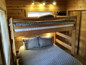 Ein Etagenbett mit gemustertem Kissen und Matratze, Holzwänden und einem Fenster mit Jalousien.